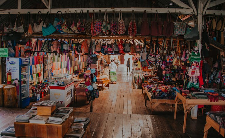 A colorful array of handcrafted bags and textiles in a lively indoor market setting.